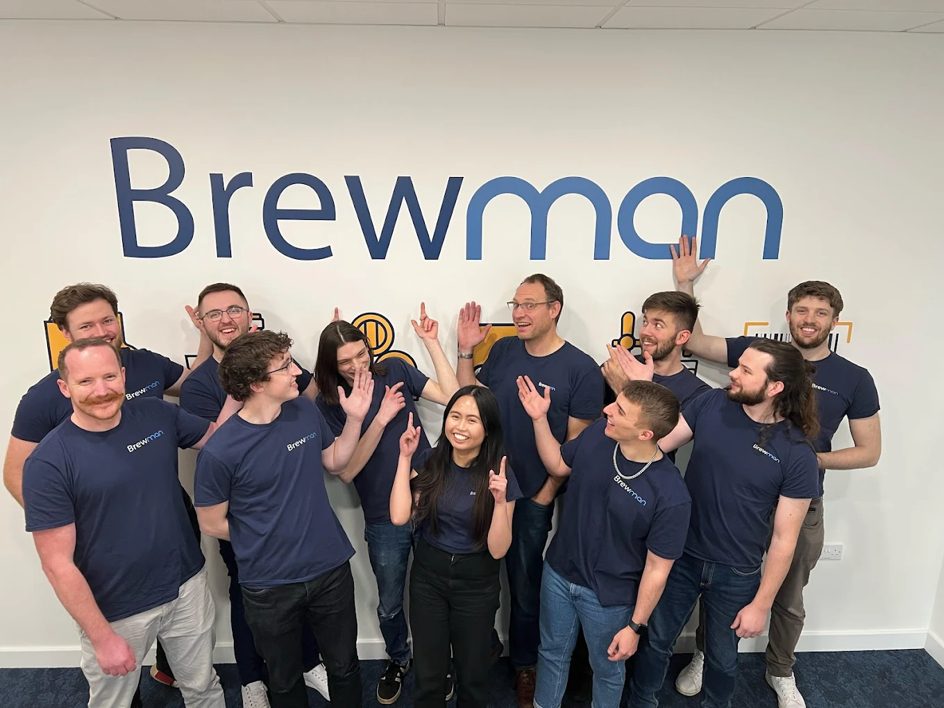 Brewman team posing together in the office pointing at the Brewman logo